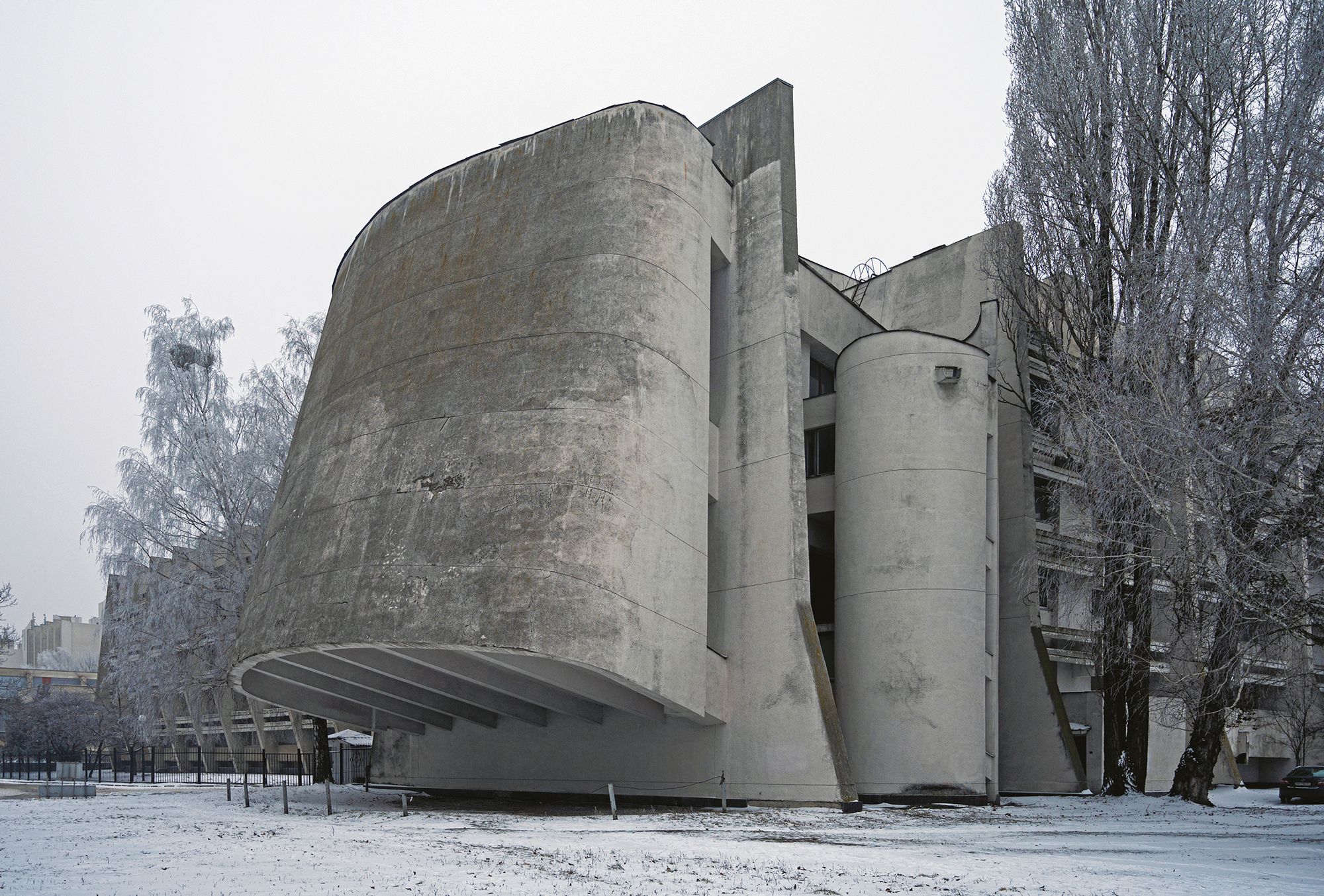 Modernist building with a curved concrete facade, surrounded by snow-covered trees in a winter landscape.