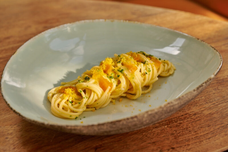 Spaghetti topped with orange zest and herbs, served on a light blue plate against a wooden background.