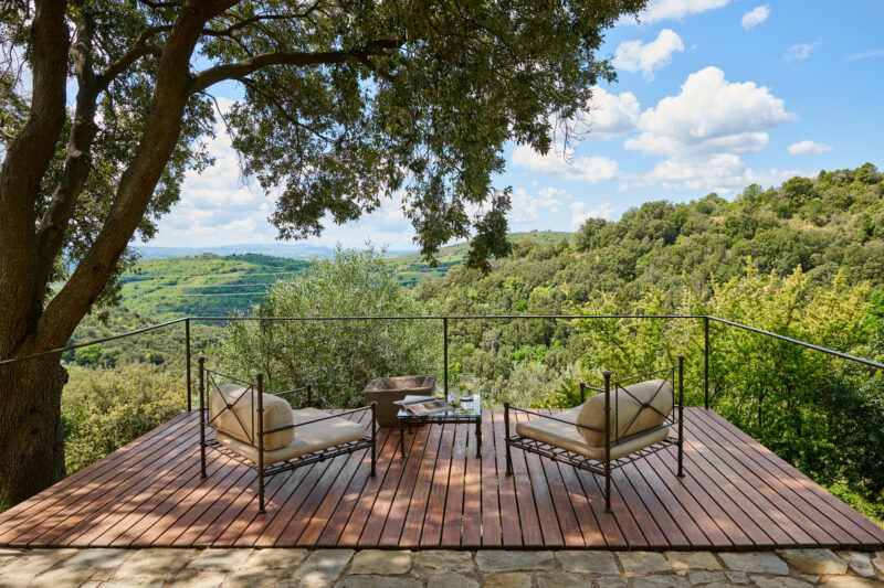 Two chairs on a wooden deck overlooking a lush green landscape with rolling hills and a blue sky.