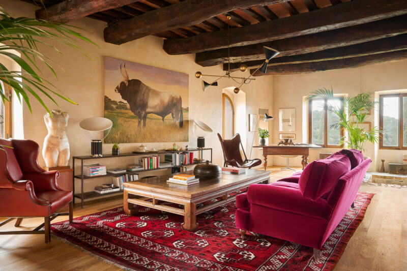 Stylish living room at Castello di Vicarello featuring a bull painting, vintage furniture, and a vibrant red rug.
