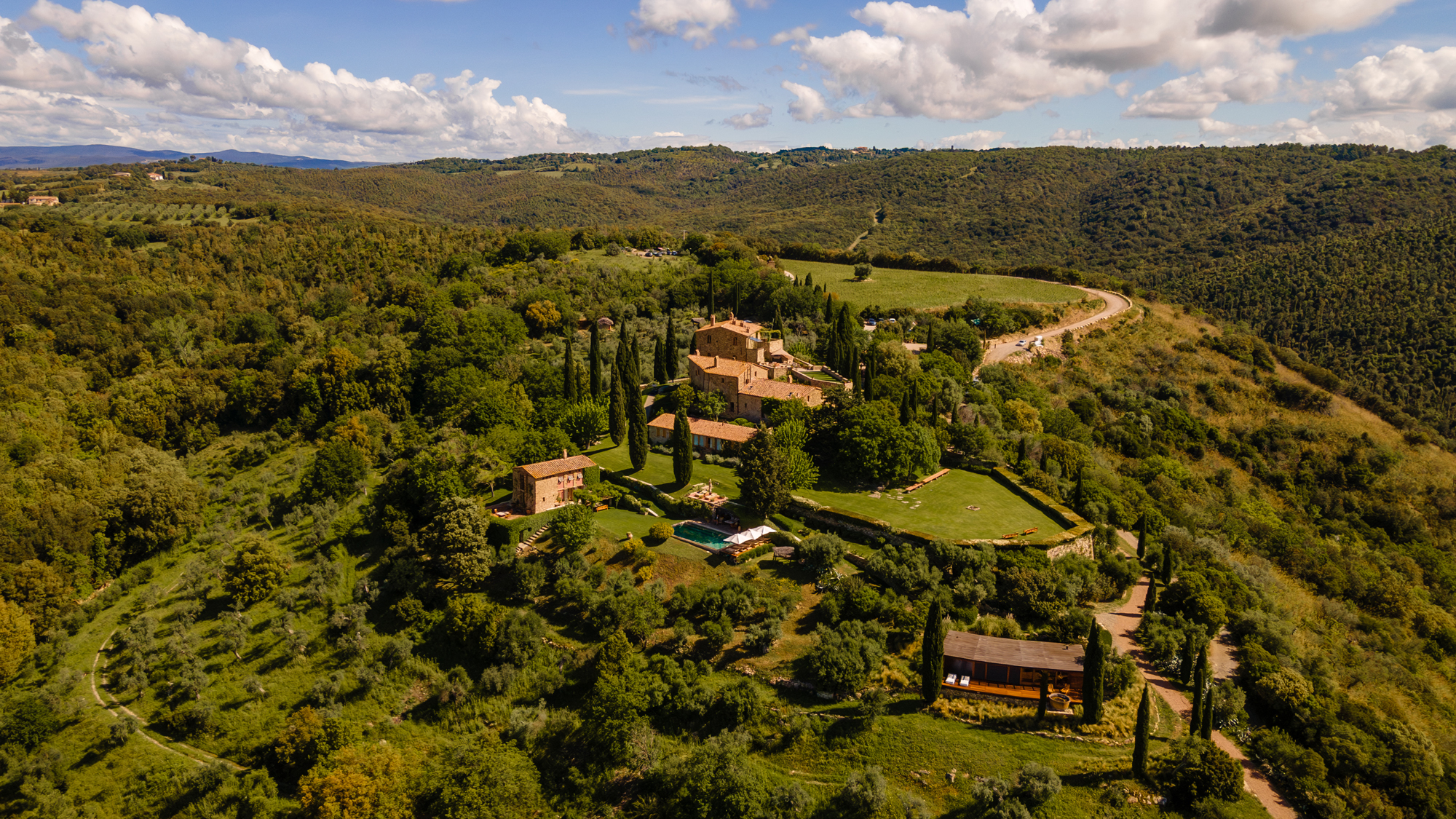 Aerial view of Castello di Vicarello, surrounded by lush greenery and rolling hills under a partly cloudy sky.