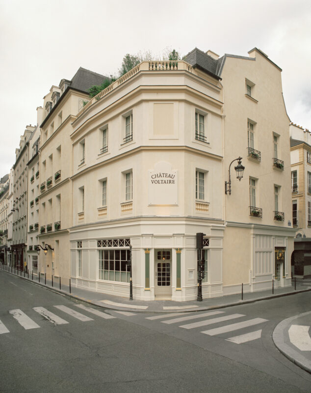 Elegant corner building of Château Voltaire in Paris, featuring cream-colored walls and decorative balconies.