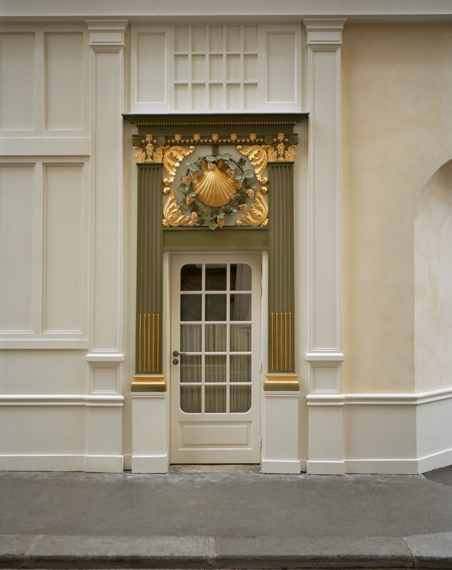 Ornate door framed by decorative columns and a shell motif, set against a light-colored wall.