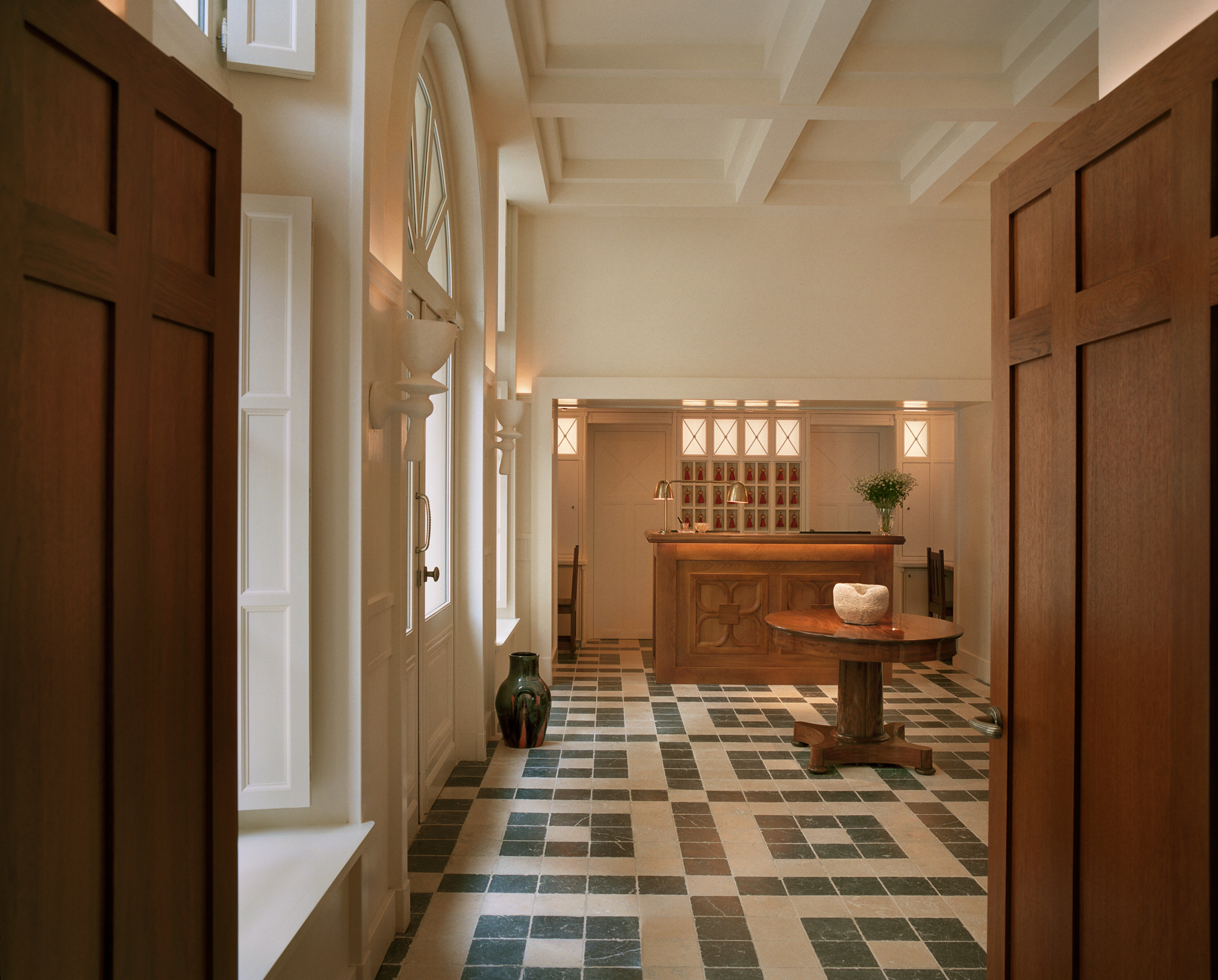 Interior of Château Voltaire featuring a wooden reception desk, tiled floor, and natural light from large windows.