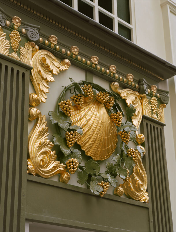 Ornate golden shell and grapevine decoration on a wall, showcasing intricate craftsmanship at Château Voltaire.