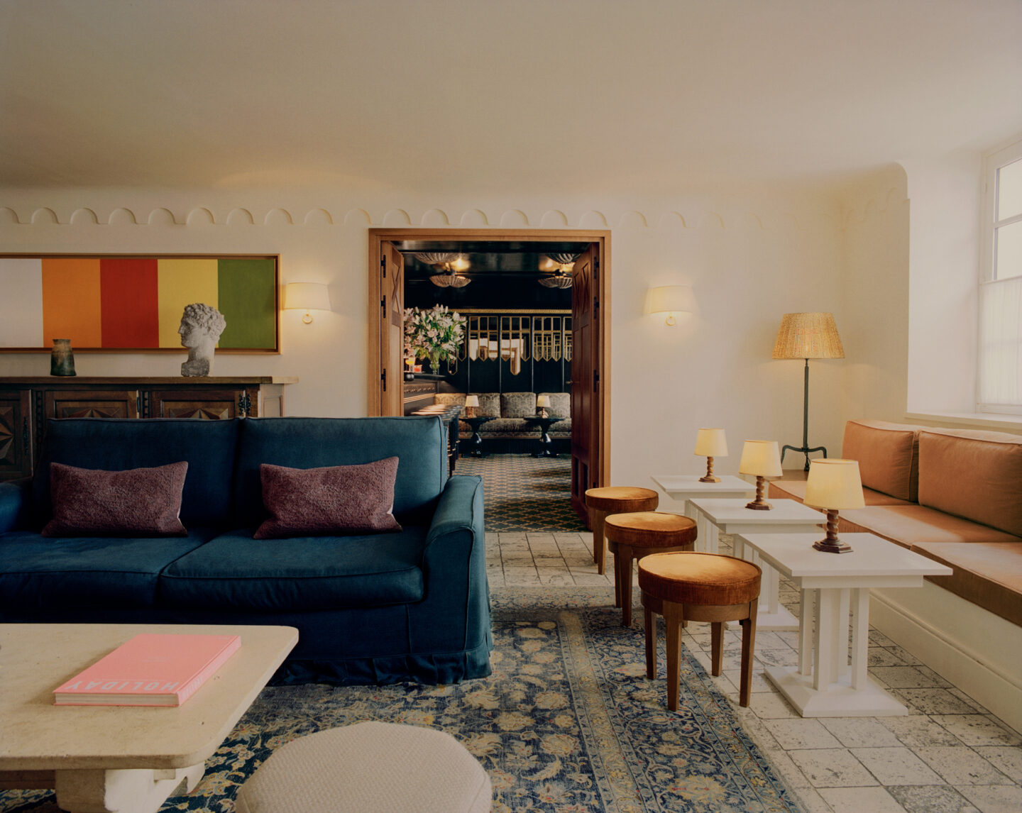 Elegant interior of Château Voltaire featuring a blue sofa, wooden tables, and warm lighting, with a glimpse of a dining ...