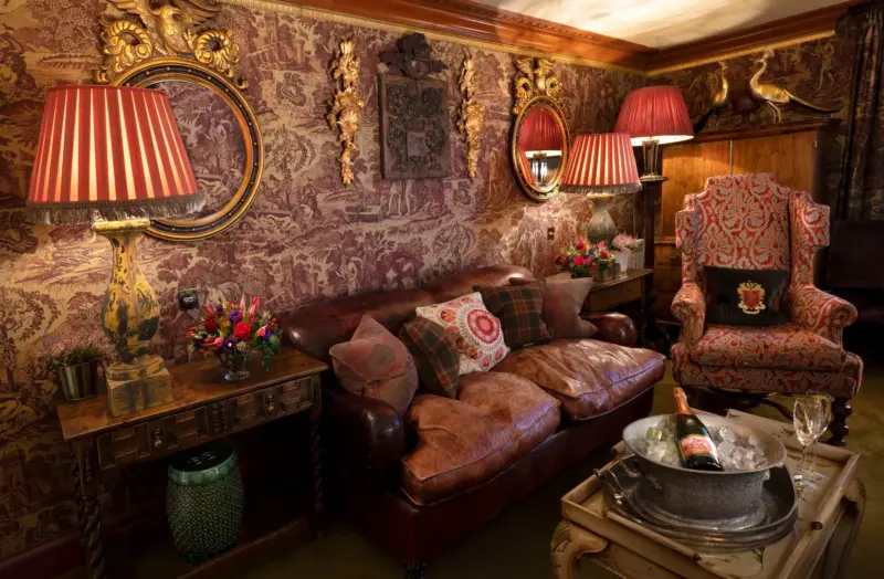 Luxurious sitting area in Prestonfield House with leather sofa, ornate armchair, floral wallpaper, and decorative lamps.
