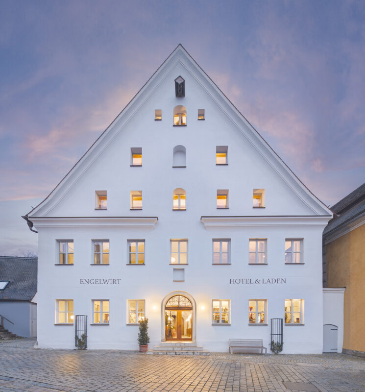White hotel building with multiple windows, featuring the name "Engelwirt Hotel & Laden" prominently displayed.