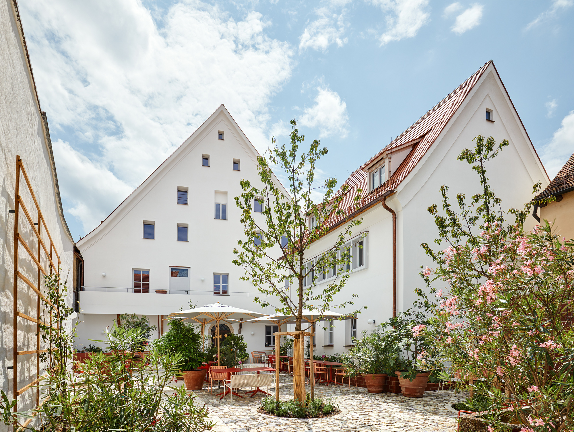 Bright courtyard of Engelwirt Hotel featuring potted plants, outdoor seating, and a white building with a sloped roof.
