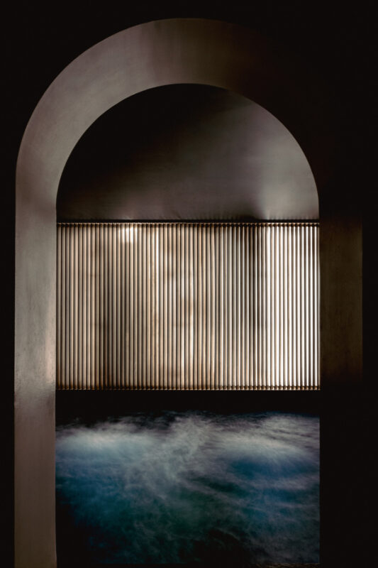 Dimly lit archway framing vertical wooden slats with soft blue fog below, evoking a serene atmosphere.