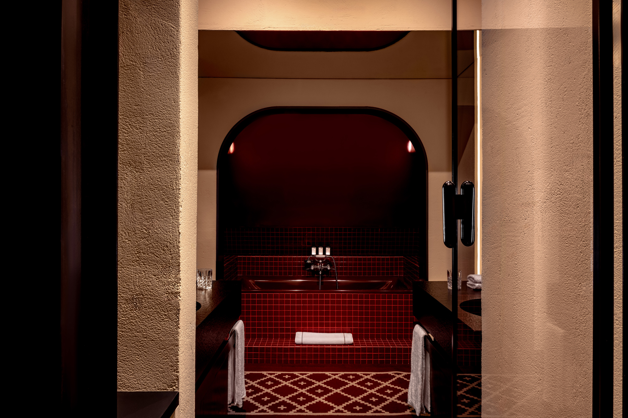 Luxurious bathroom with red tiled walls, a deep bathtub, and elegant fixtures, framed by arched openings.