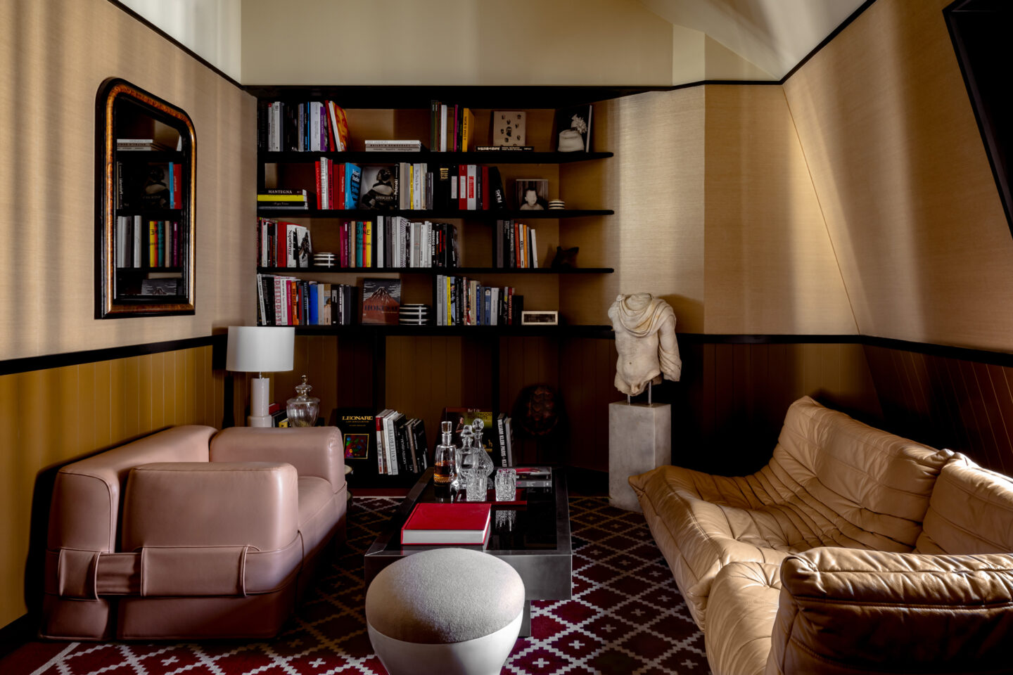 Stylish interior featuring a pink sofa, a beige couch, bookshelves filled with books, and a decorative sculpture.