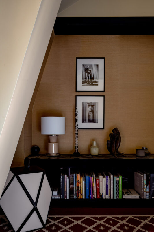 Modern interior featuring a bookshelf with books, a lamp, and framed black-and-white photographs on a textured wall.