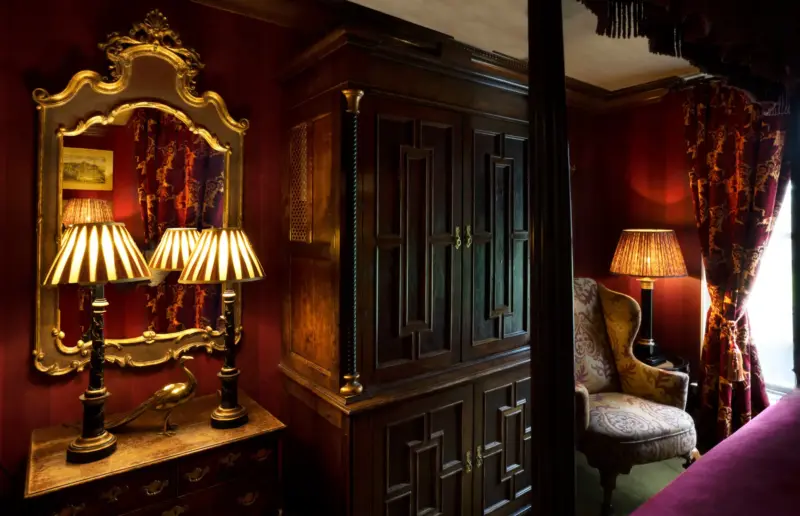 Luxurious interior of a room at Prestonfield House featuring ornate wooden furniture, lamps, and rich red walls.