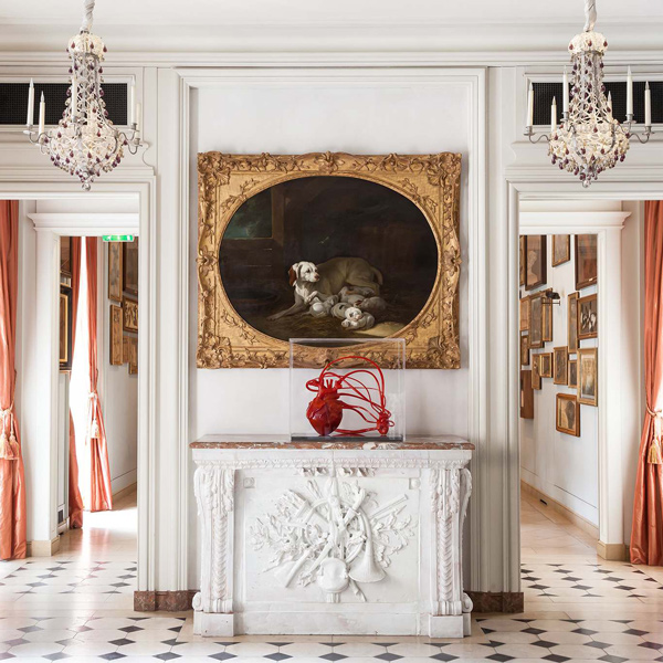 Elegant interior of a museum featuring a large painting of dogs, a modern red sculpture, and ornate chandeliers.