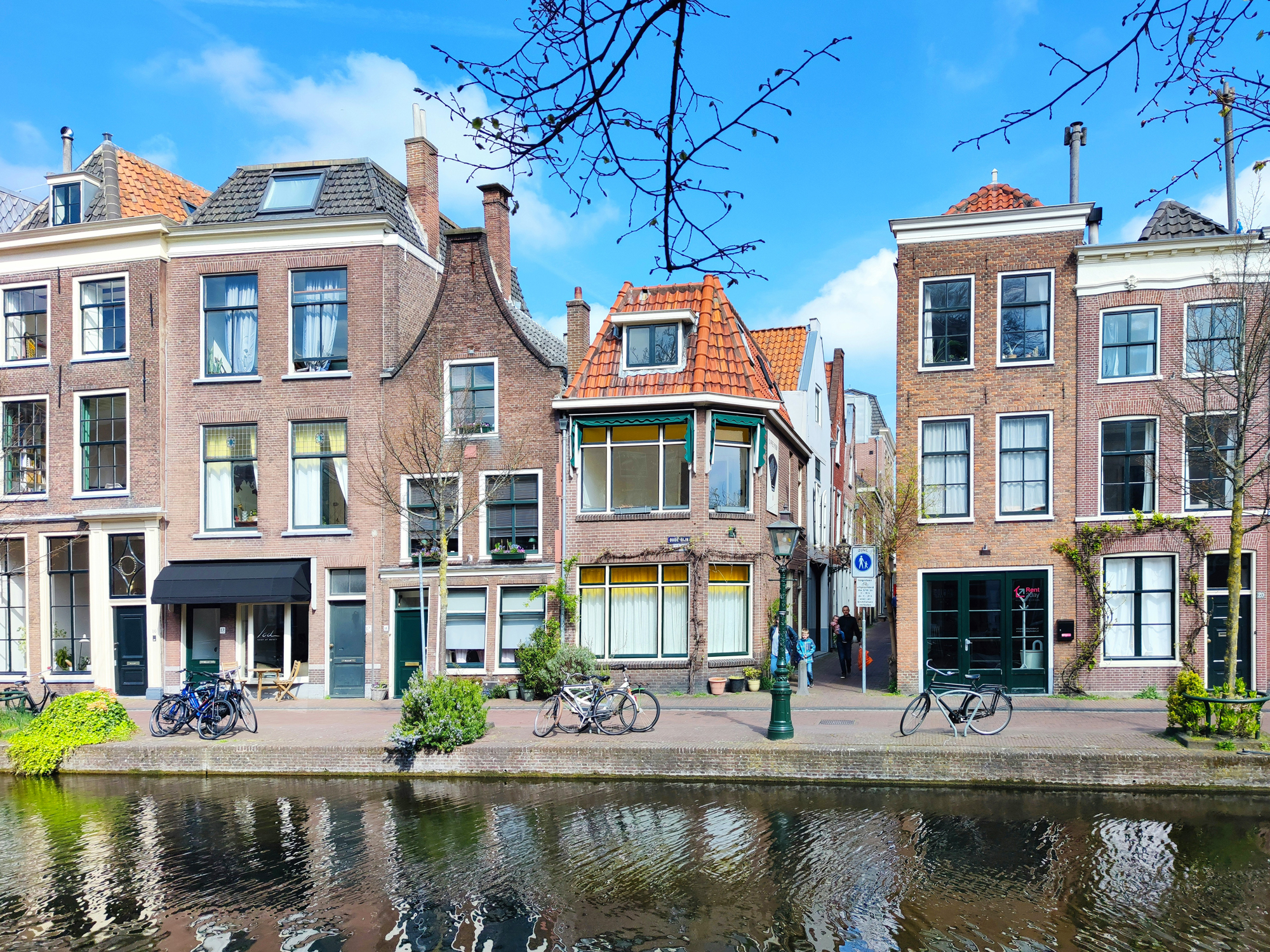 Charming canal-side houses with bicycles parked, reflecting blue sky and trees in the water, in a Dutch city.
