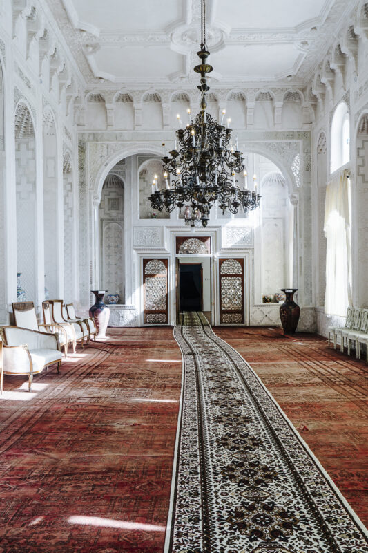 Luxurious interior of a grand room in Uzbekistan, featuring ornate chandeliers, intricate wall designs, and a patterned ca...
