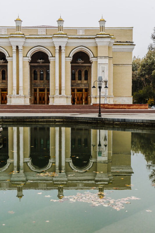 Architectural building with columns reflected in a calm pond, surrounded by autumn leaves, in Uzbekistan.