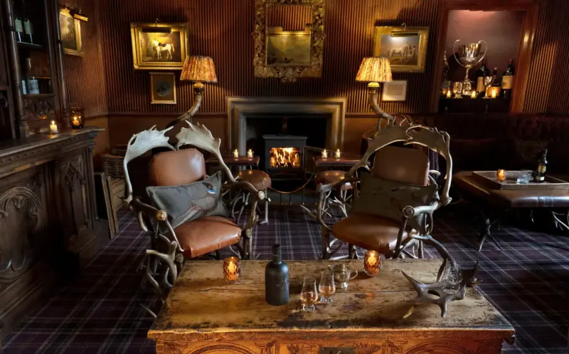 Elegant lounge at Prestonfield House featuring antler chairs, a fireplace, and whisky glasses on a decorative table.