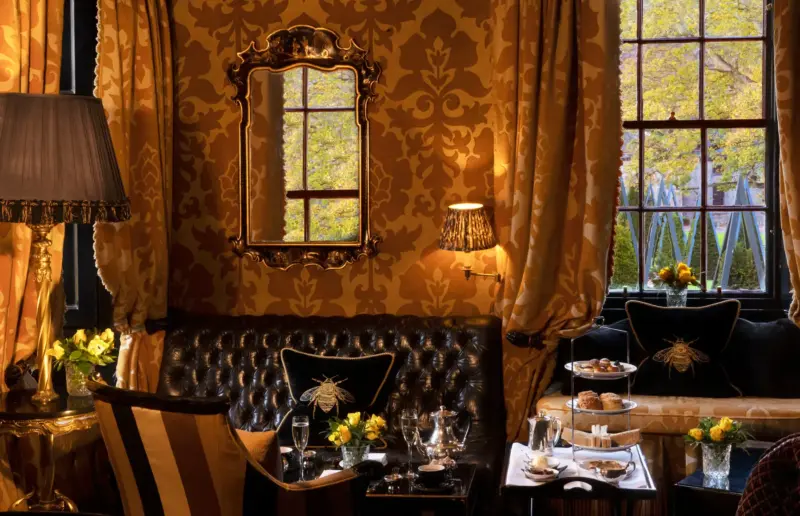 Elegant interior of the yellow room at Prestonfield House, featuring ornate decor, a mirror, and a view of autumn trees ou...