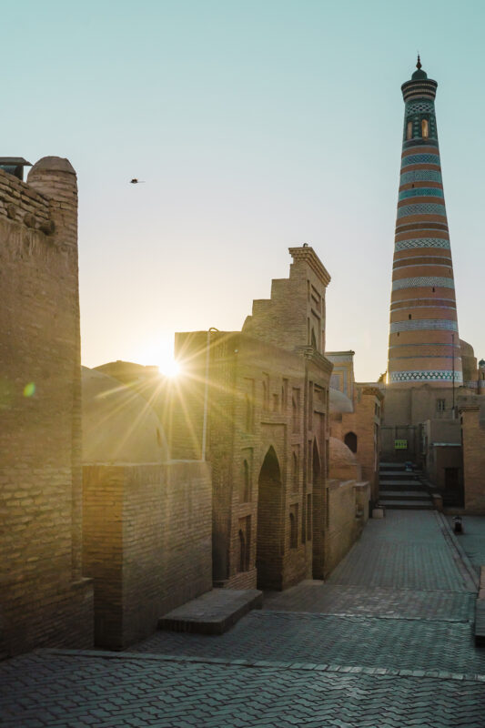 Sunrise over the ancient city of Khorezm, featuring a colorful minaret and historic brick buildings.