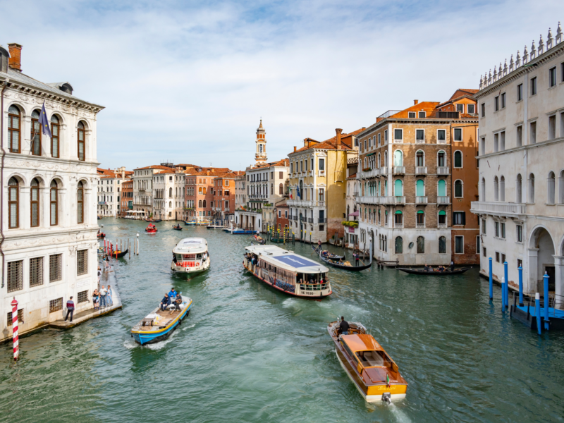 Canal in Venice with boats navigating through historic buildings under a blue sky.