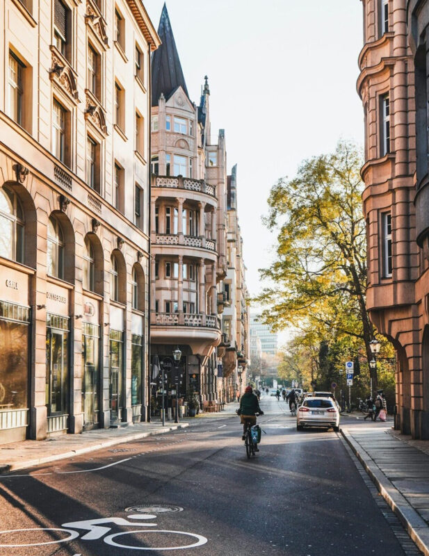 Bicyclist riding on a street lined with historic buildings and trees, bathed in warm sunlight.