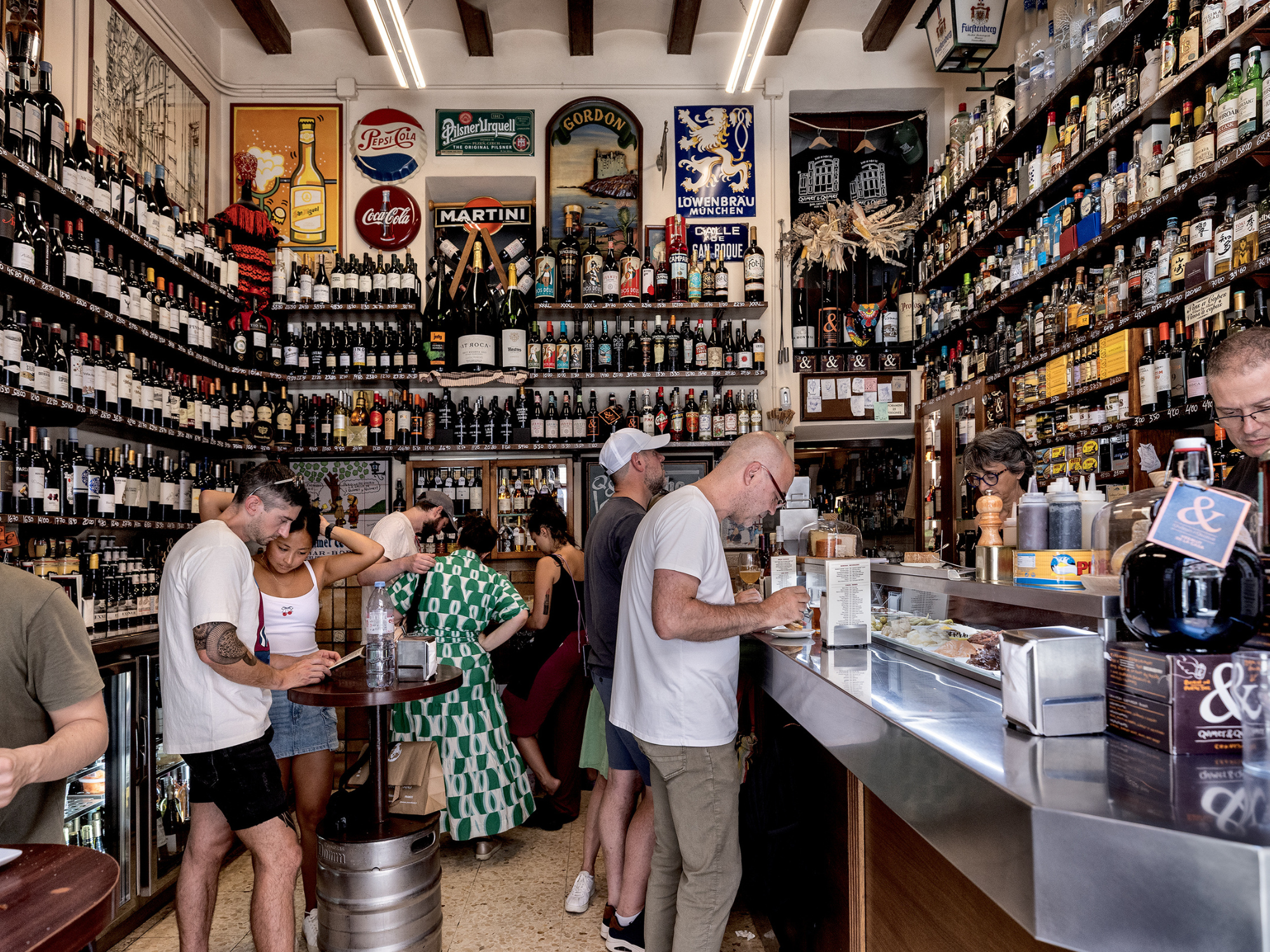 A bustling bar in Barcelona filled with shelves of various wines and spirits, patrons enjoying drinks and conversation.