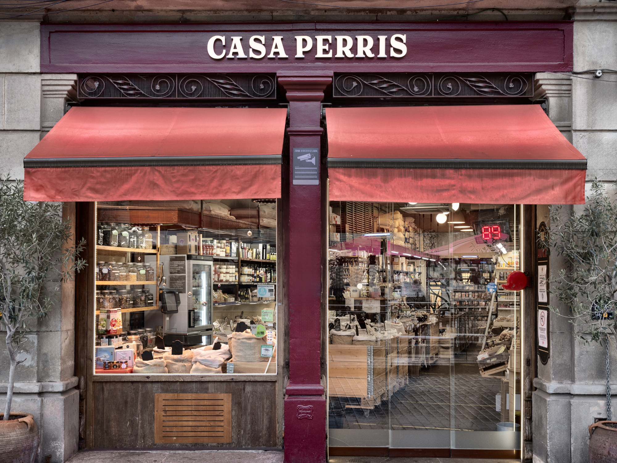 Storefront of Casa Perris in Barcelona, featuring large windows displaying various products and red awnings.
