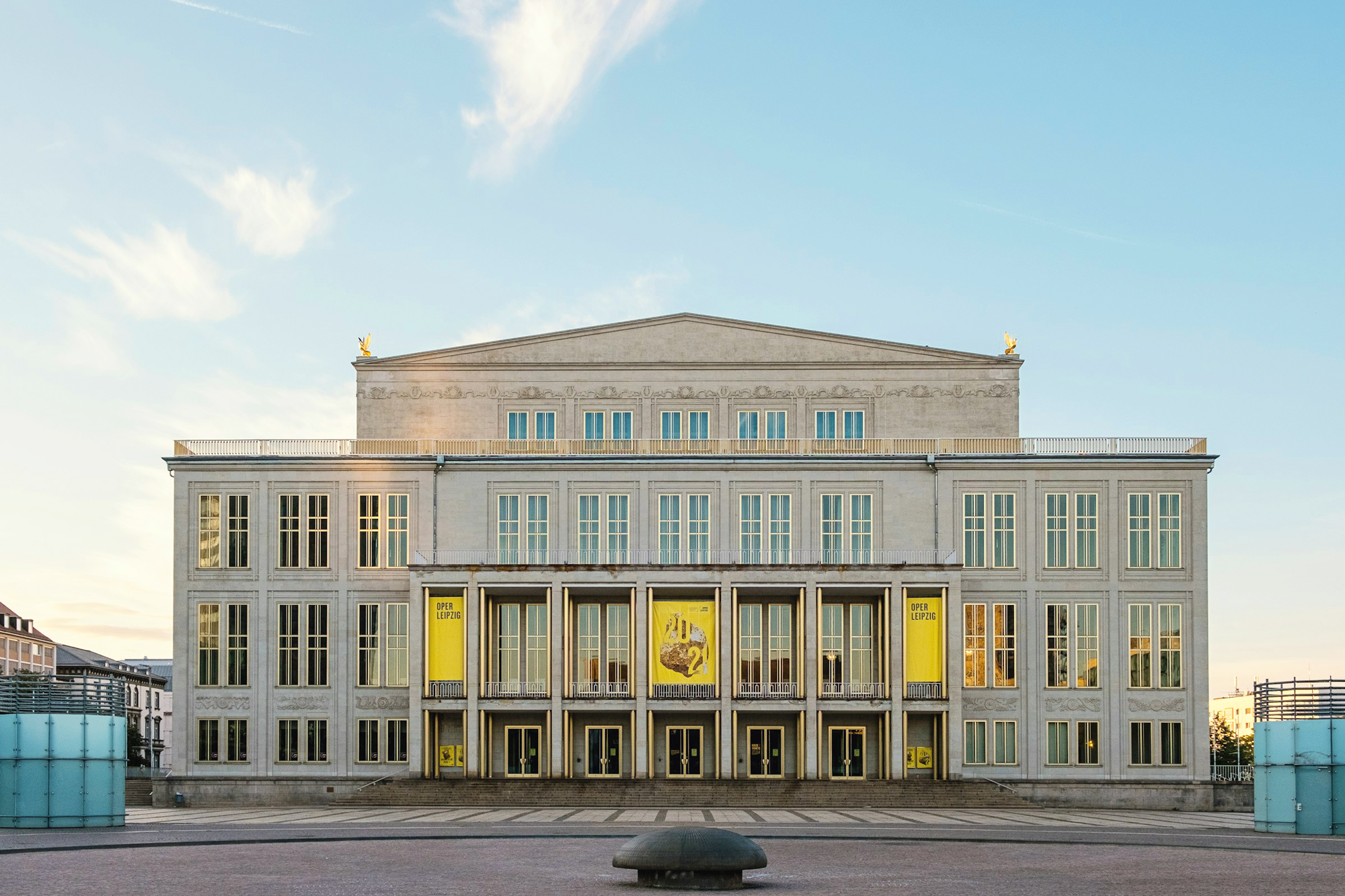 Neoclassical building facade with large windows, yellow banners, and a clear blue sky in the background.