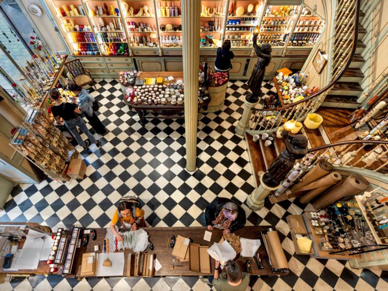 Colorful shelves filled with art supplies in a bustling store, with customers and staff engaged in various activities.