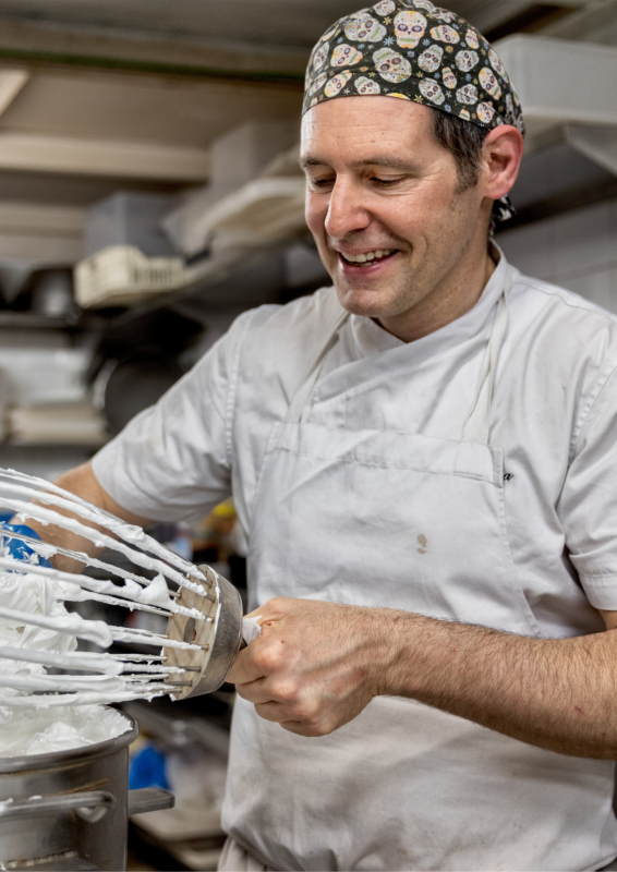 Chef in a kitchen, smiling while using a mixer to whip cream.