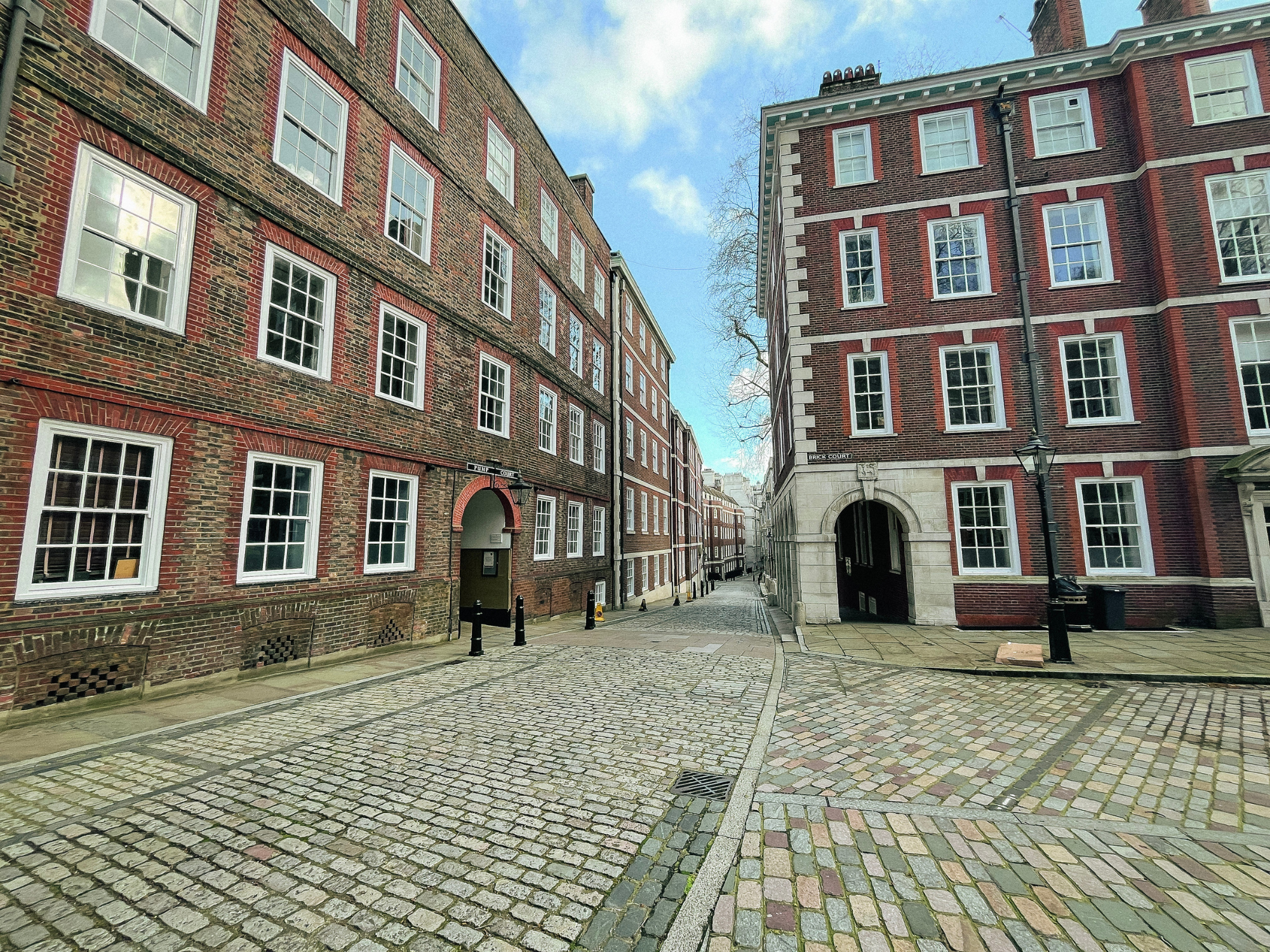 Cobblestone street lined with red-brick buildings in London, featuring large windows and a clear blue sky.