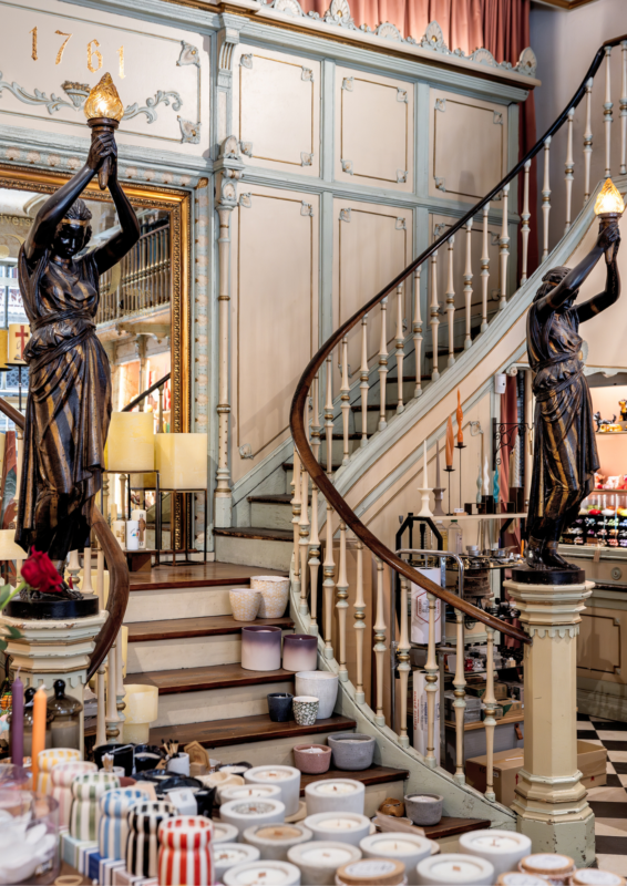 Elegant staircase with two statues holding lamps, surrounded by decorative candles and pottery in a stylish shop.
