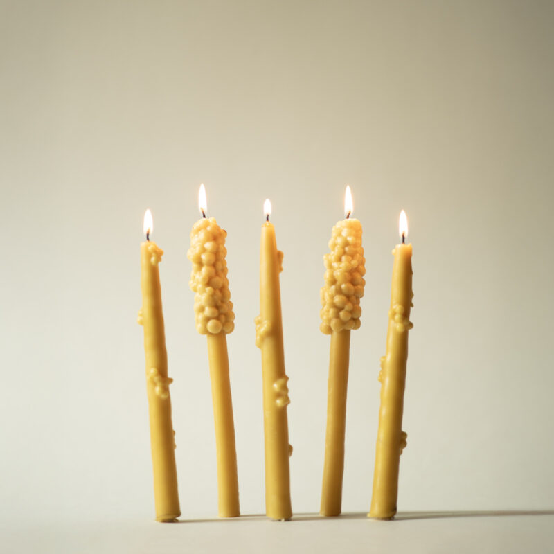 Five lit beeswax candles with textured tops, standing against a light beige background.
