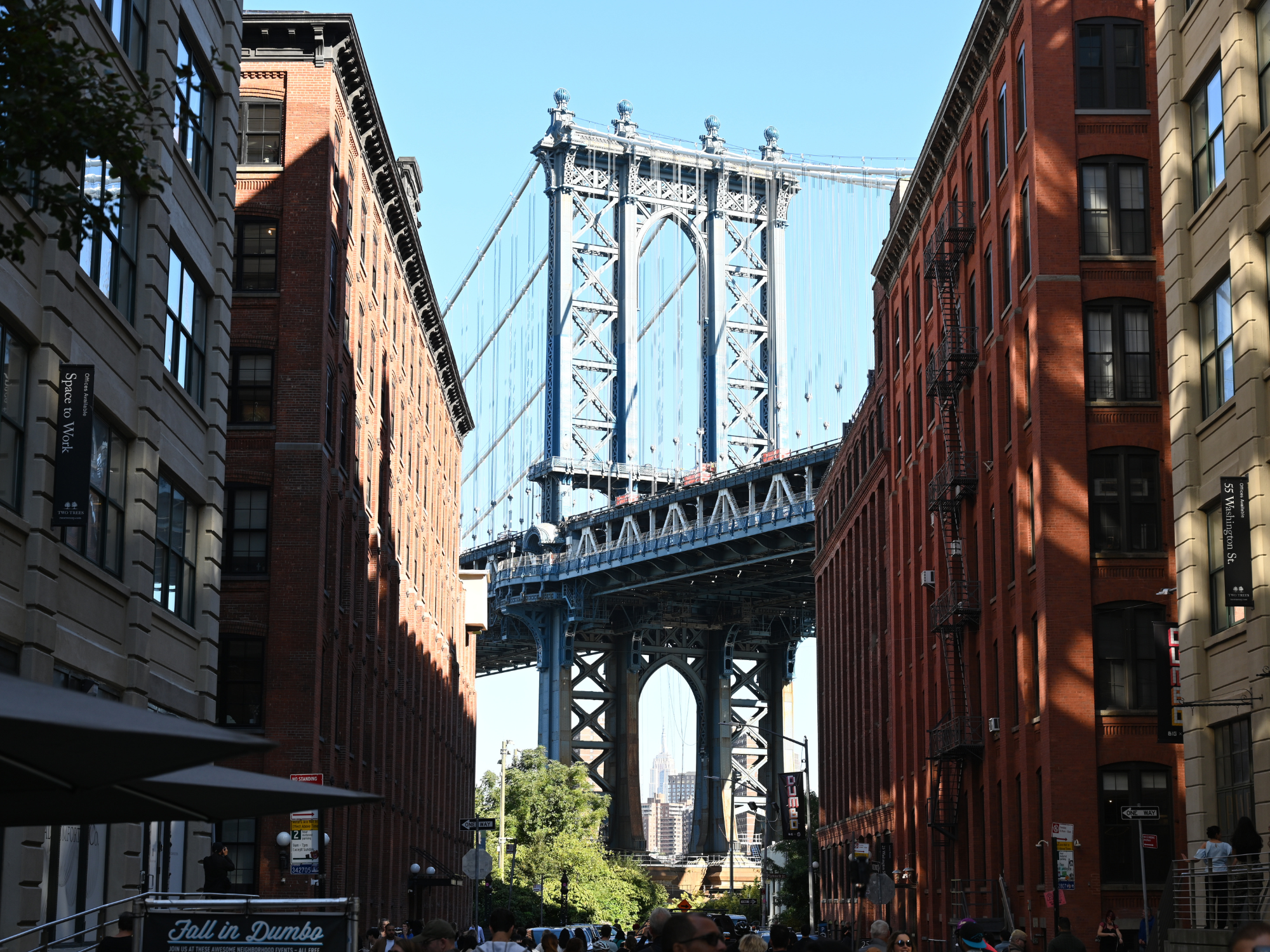 View of the Manhattan Bridge framed by red brick buildings and a clear blue sky in Dumbo, Brooklyn.