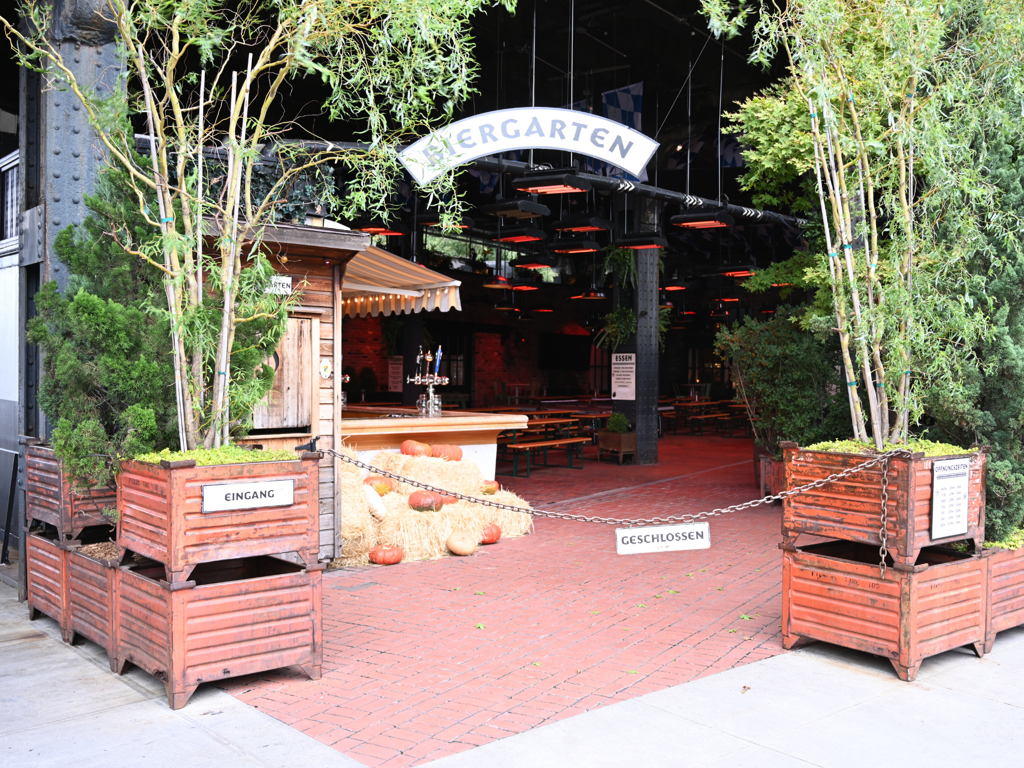 Entrance to a closed beer garden with wooden planters, pumpkins, and a sign indicating "EINGANG" and "GESCHLOSSEN.