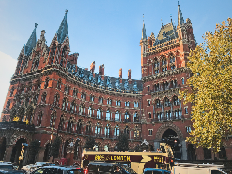 St. Pancras International, a Victorian Gothic railway station, with a double-decker bus in front and autumn trees nearby.