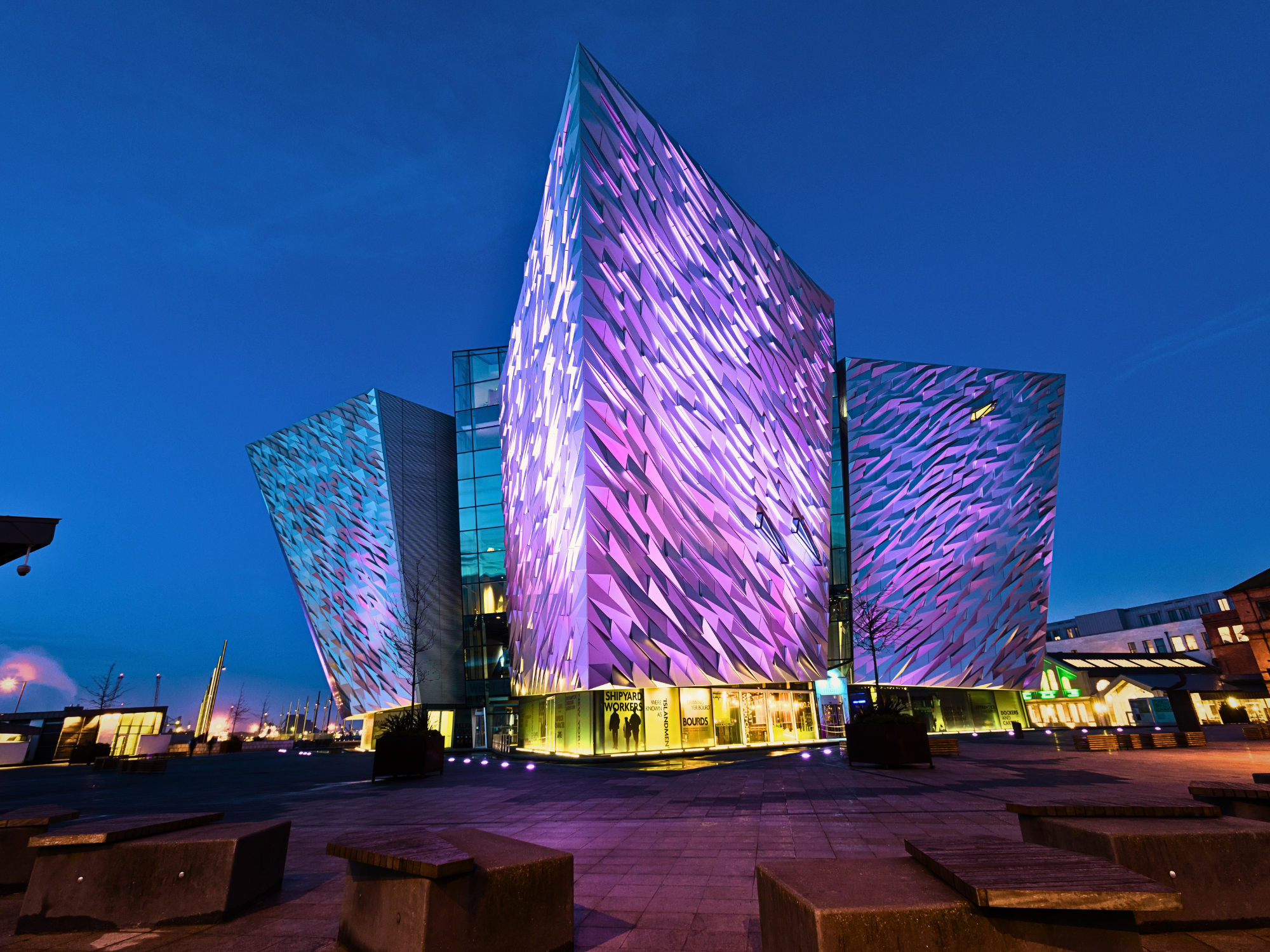 Modern building with a striking, illuminated facade in shades of purple and blue, set against a twilight sky in Ireland.