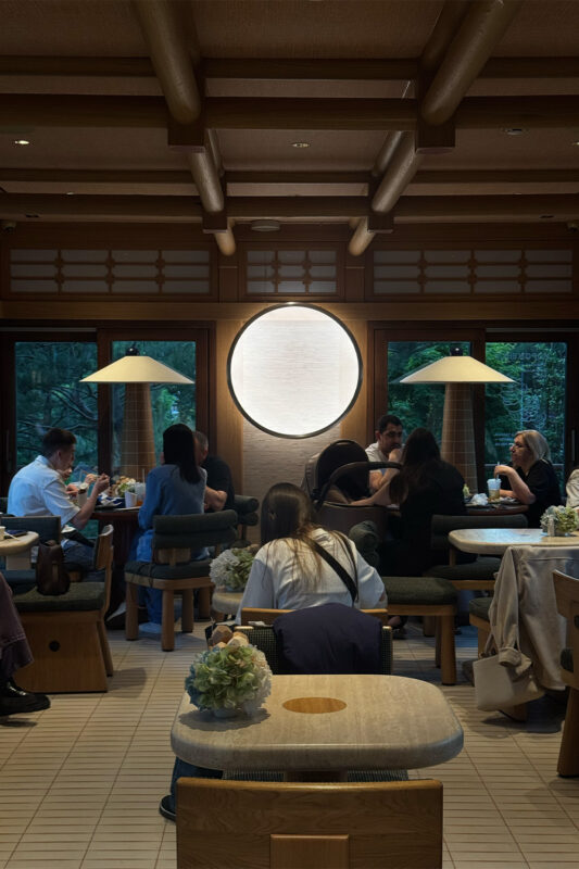 Interior of a café with patrons seated at wooden tables, large round window, and soft lighting.