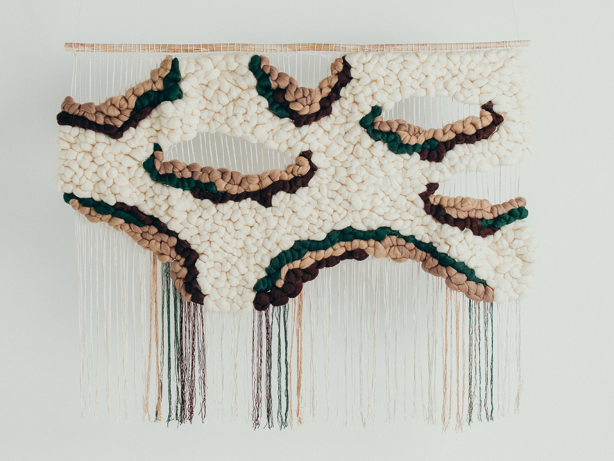 Textile wall hanging featuring abstract shapes in cream, brown, green, and black, with hanging threads.