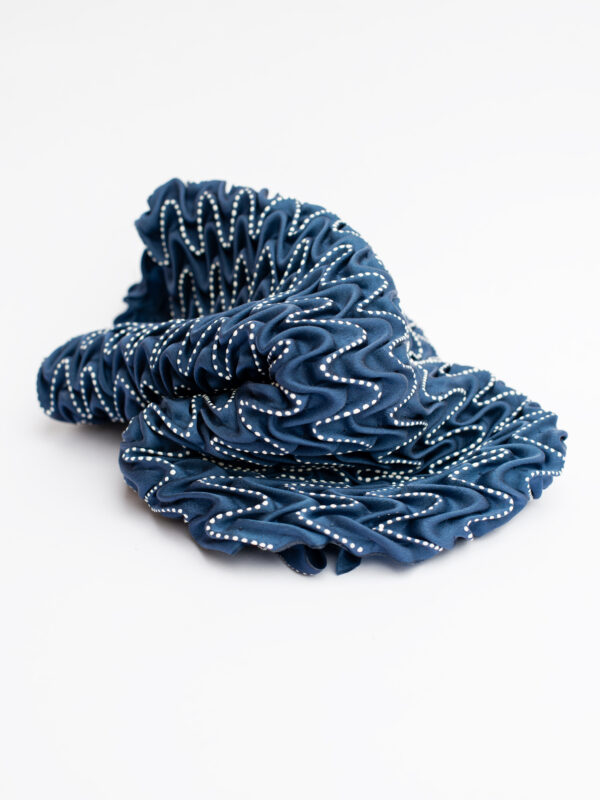 Navy blue fabric with a wavy texture and white bead embellishments, arranged in a loose, crumpled shape.