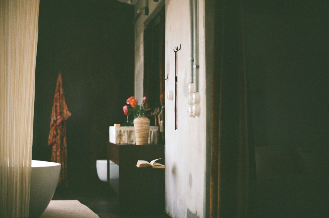 A softly lit bathroom featuring a freestanding tub, a wooden vanity with flowers, and a book on the floor.