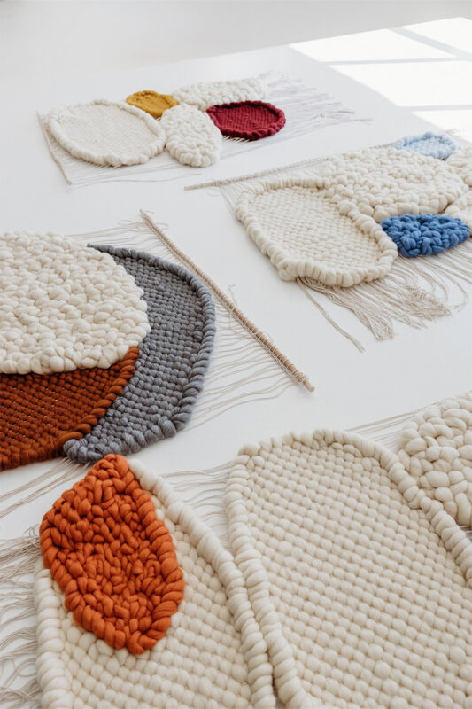 Textured wall hangings in various colors and shapes, arranged on a light surface with natural lighting.