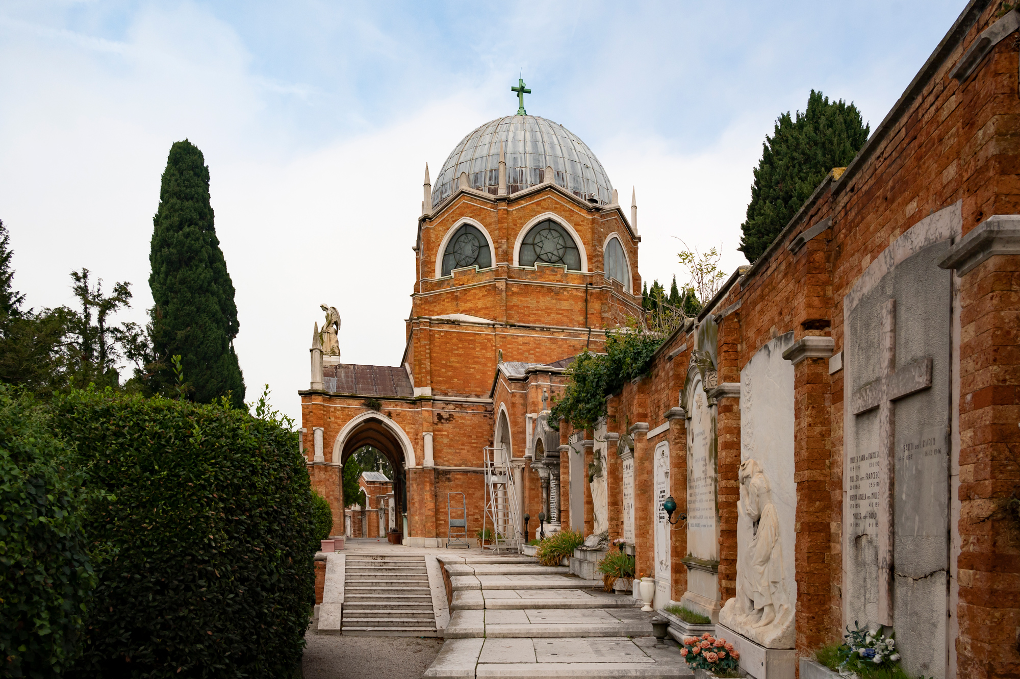 Historic cemetery in Venice featuring a domed building and stone sculptures along a pathway.