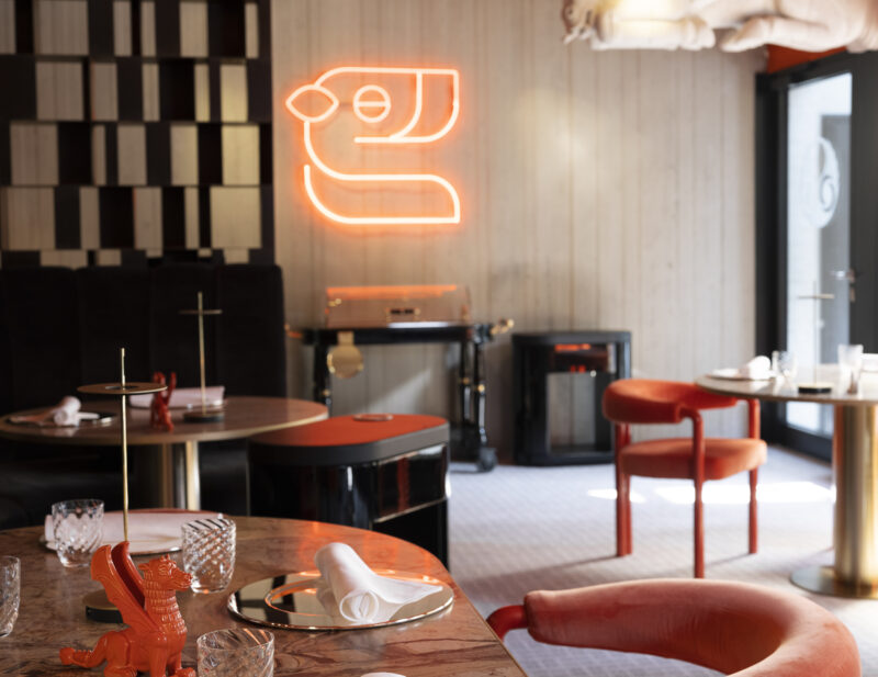 Interior of Tantris DNA restaurant featuring a neon logo, elegant tables, and modern decor in warm tones.