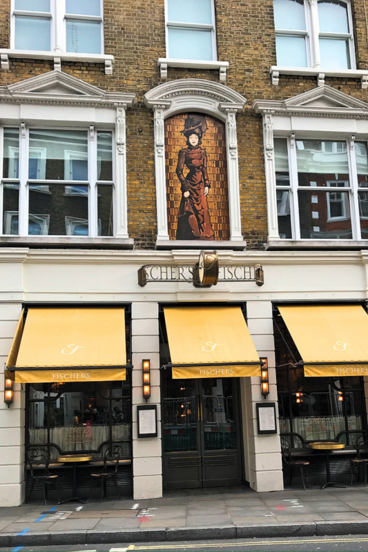 Facade of a restaurant in London featuring a large mural of a woman above the entrance and yellow awnings.