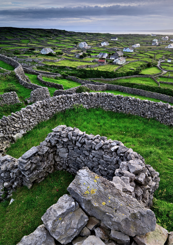Stone walls and green fields with scattered white houses under a cloudy sky, depicting a rural Irish landscape.