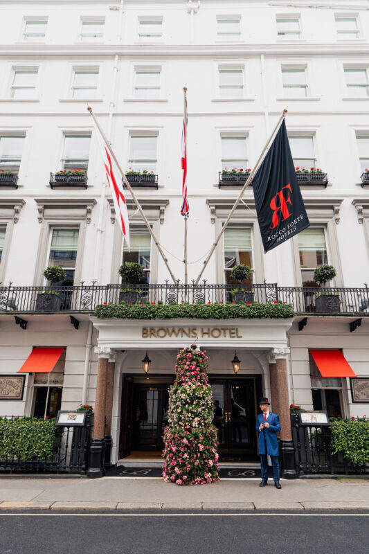 Facade of Brown's Hotel featuring floral arrangements, flags, and a doorman in uniform.