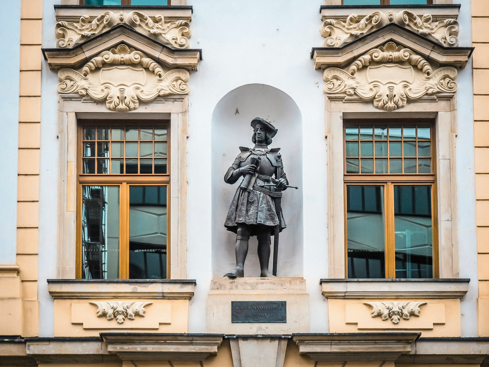 Statue of a historical figure in ornate architectural niche between two windows on a building in Leipzig.